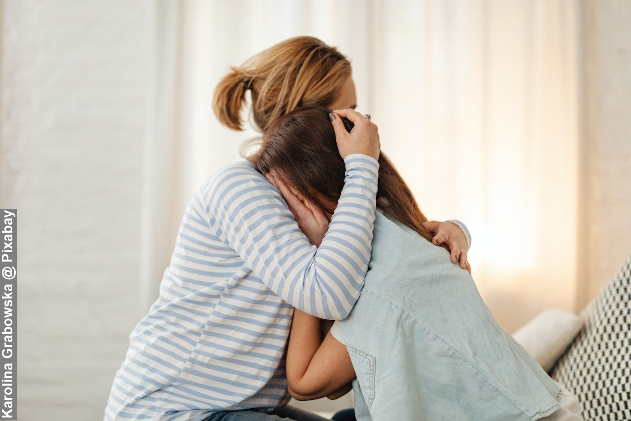 Mother comforting crying daughter in bedroom