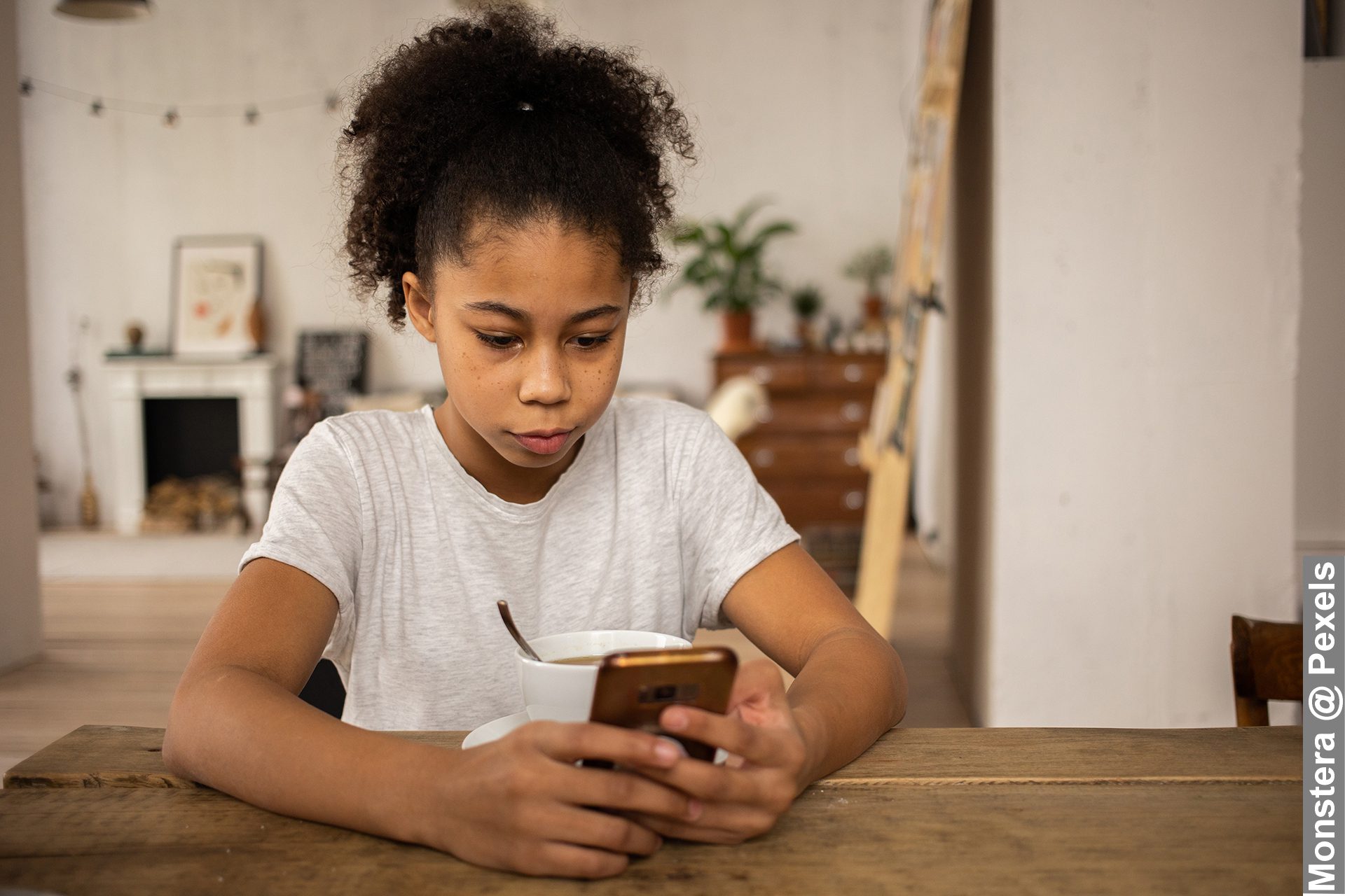 Young black girl surfing Internet on smartphone at table with coffee, need to keep children safe online