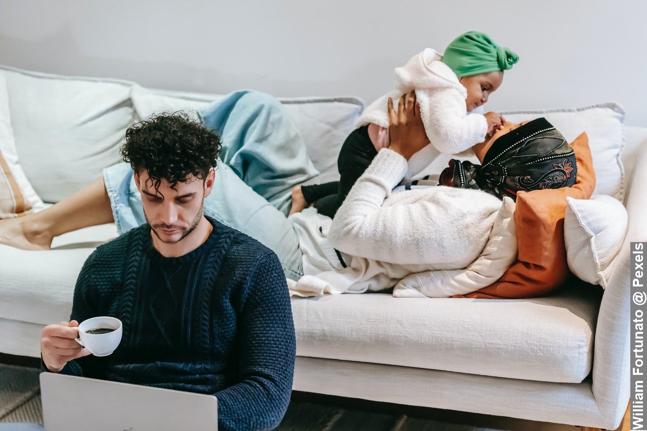 Black mother playing with baby while father working on laptop