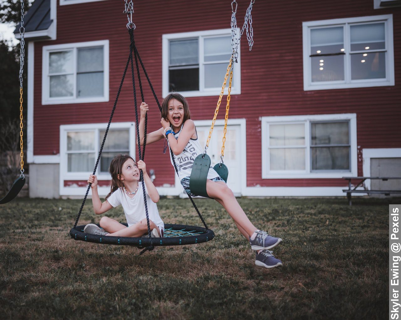 Happy girls spending time on playground near house during hot weather