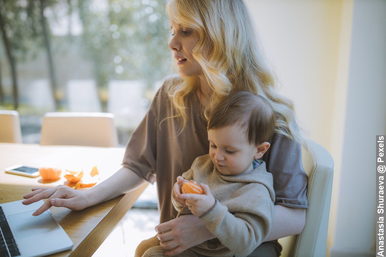 Balancing work and family life, mum carrying her baby while working on her laptop