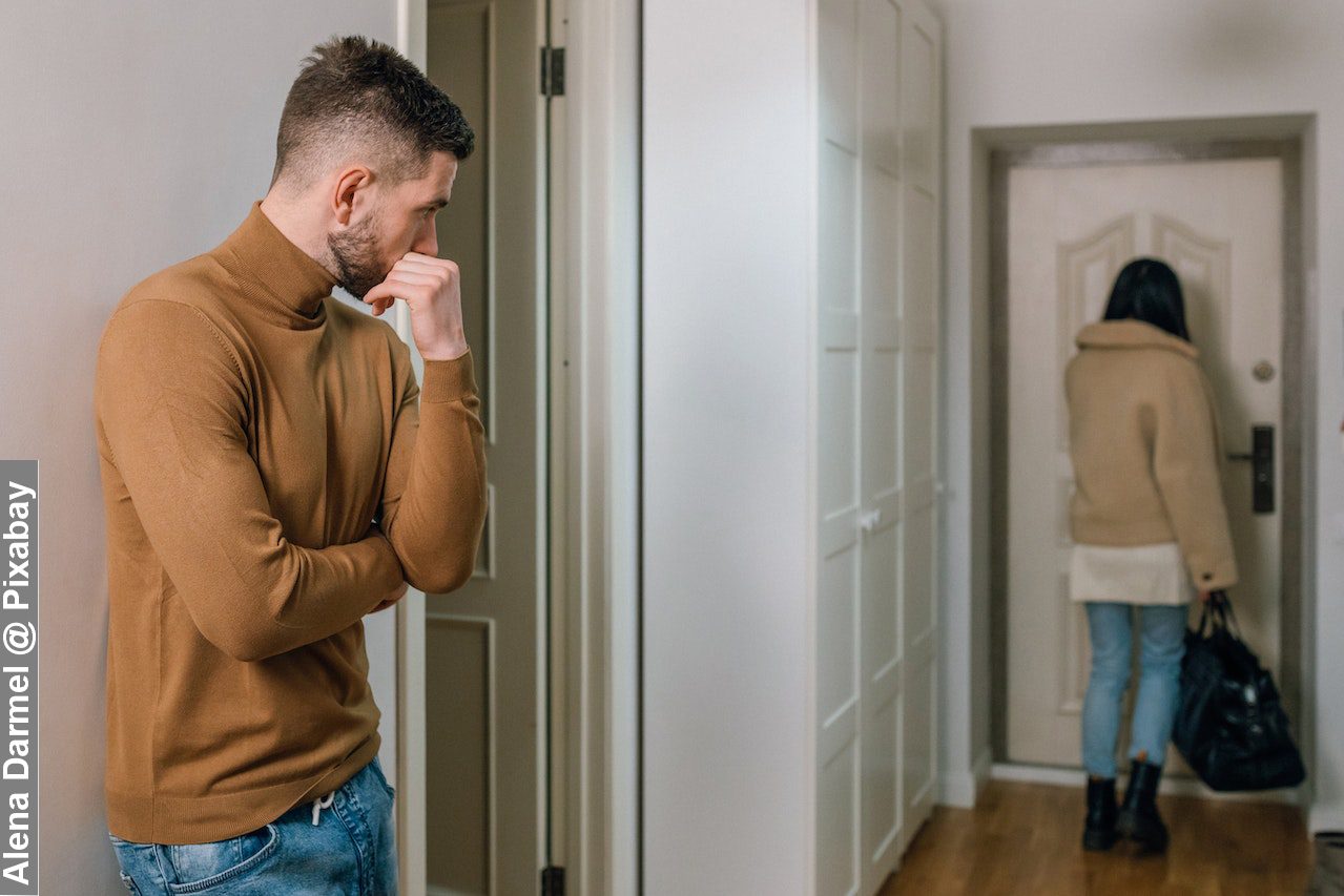 Man in brown long sleeve shirt and blue denim jeans standing near white wall after deciding to divorce