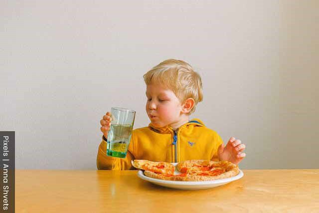 Young boy eating pizza happily, but a role of a mother is to ensure healthy eating