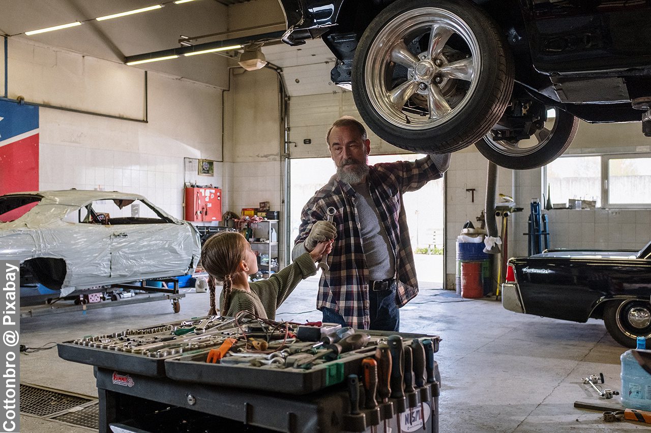 Father teaching daughter in a car garage how to fix cars