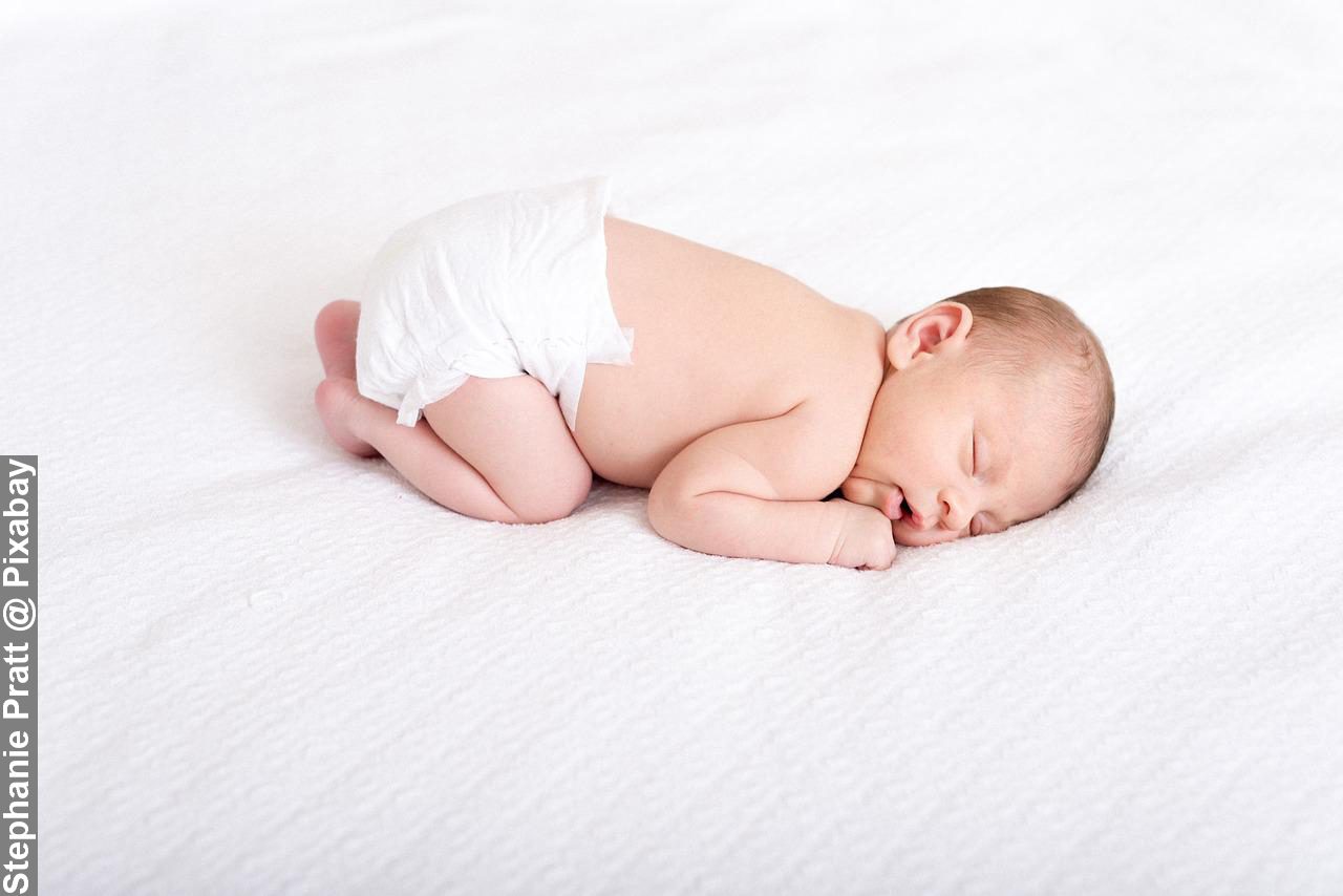 Newborn baby showing science of sleep sleeping on white bed curled up