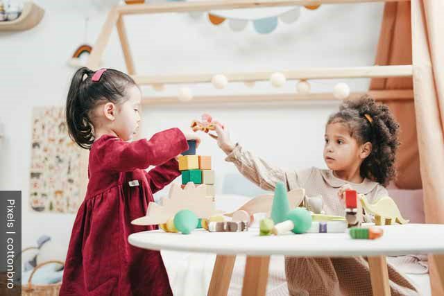 Two little girls playing with blocks around a round table