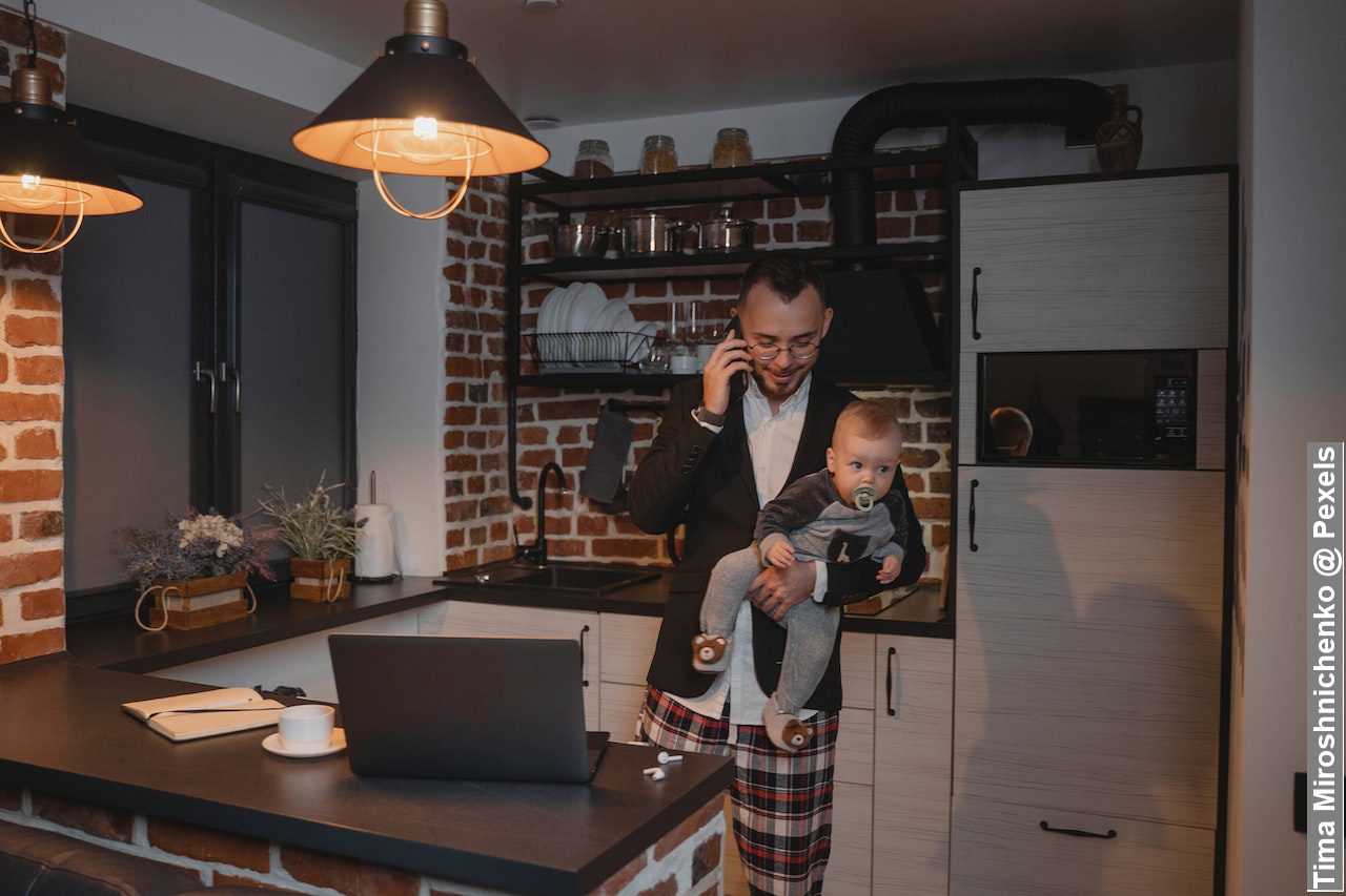 A Man in Black Suit Jacket Carrying Baby While Talking on Phone