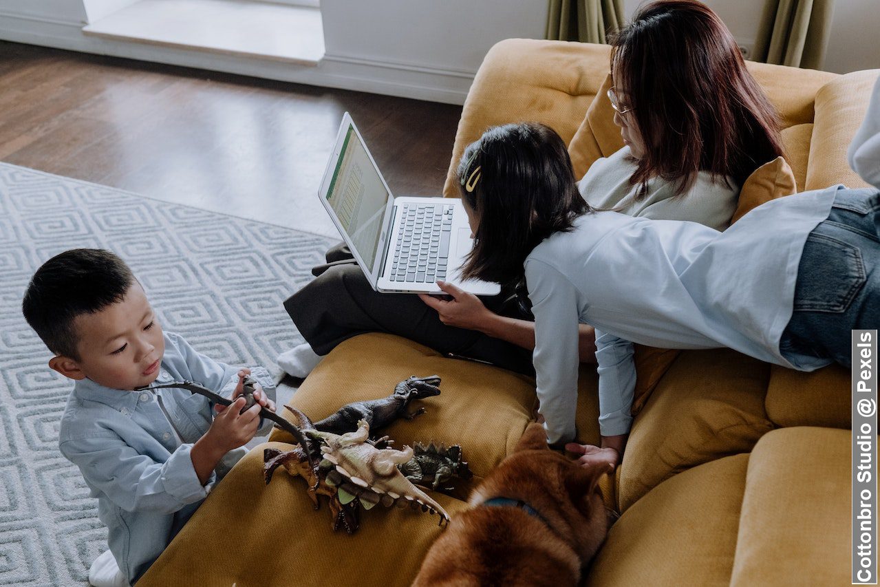 Mum working from home with kids, using her laptop with her kids playing beside her