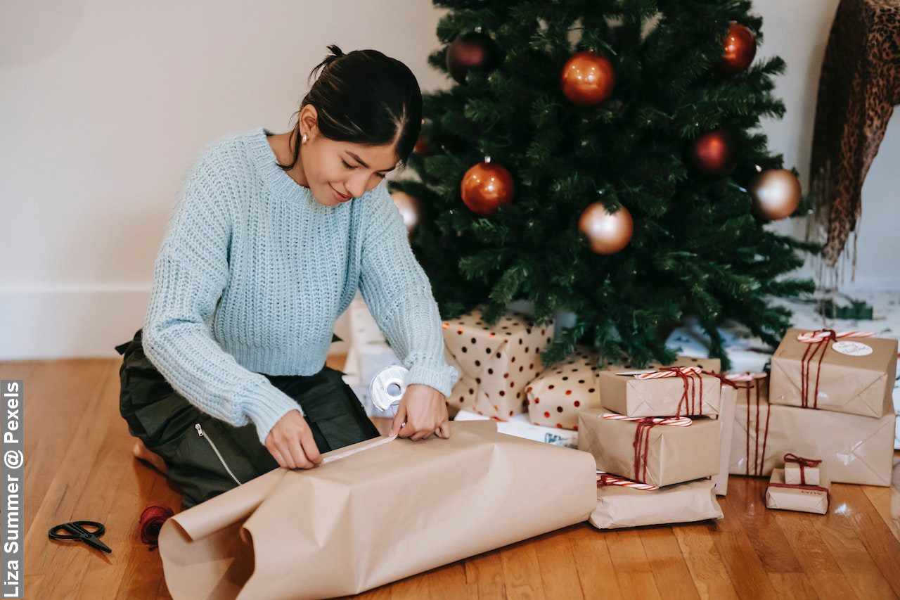 Content Asian woman wrapping present box near Christmas tree early to survive Christmas