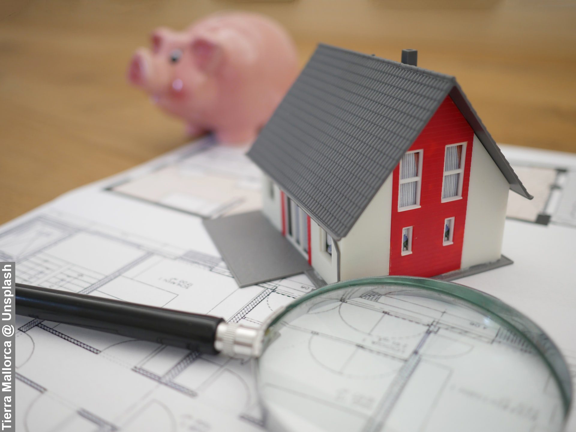 Financing balancing with magnifying glass, pink pig and model house