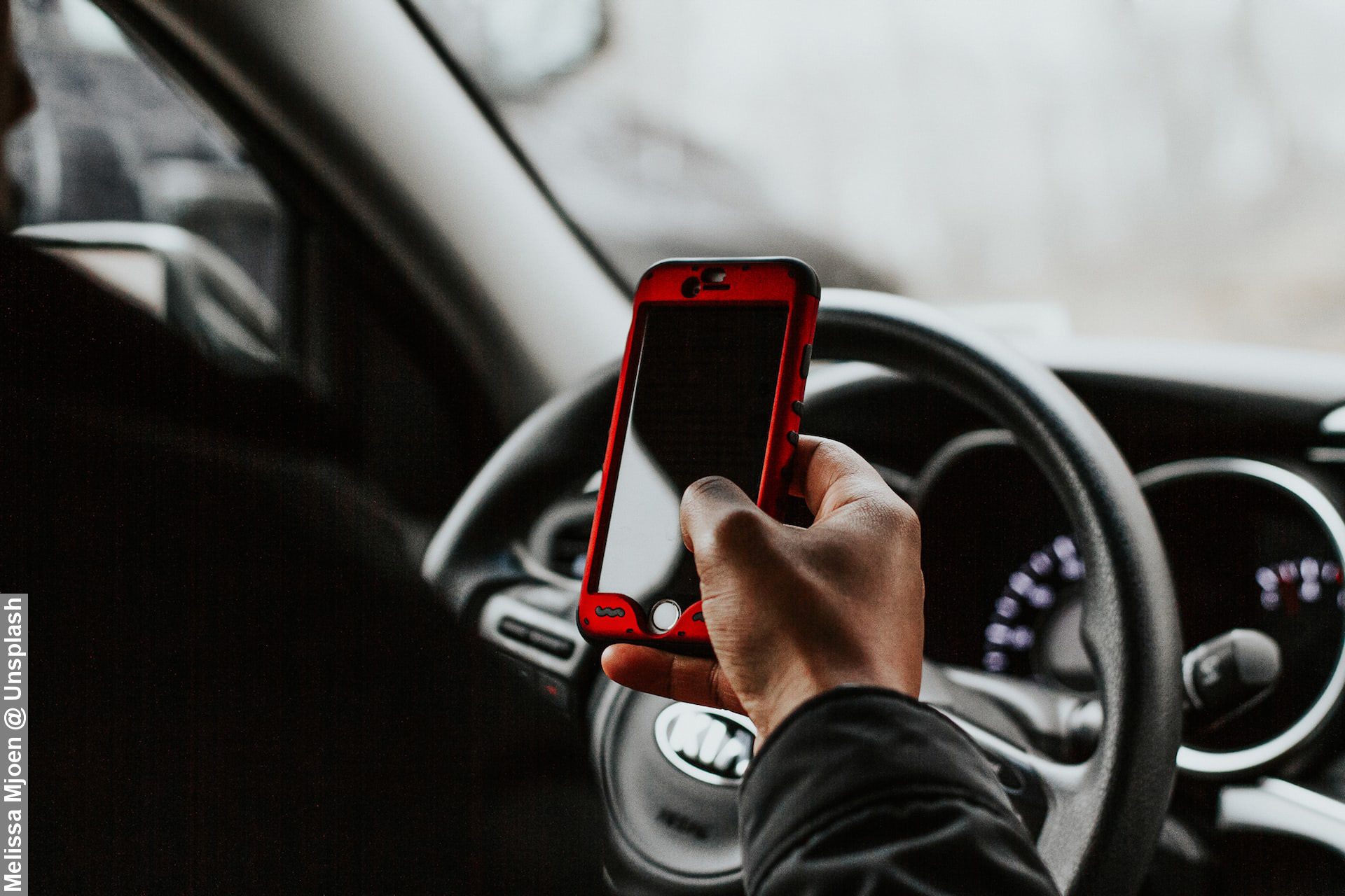 Inside a car, driver with red mobile phone next to steering wheel