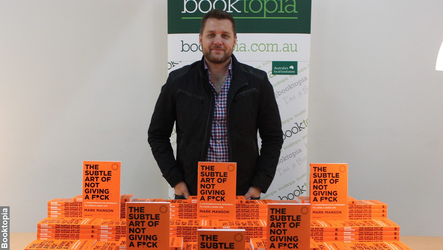 Mark Manson at book launch of The Subtle Art of Not Giving a F*ck at Booktopia, standing next to a lot of his books