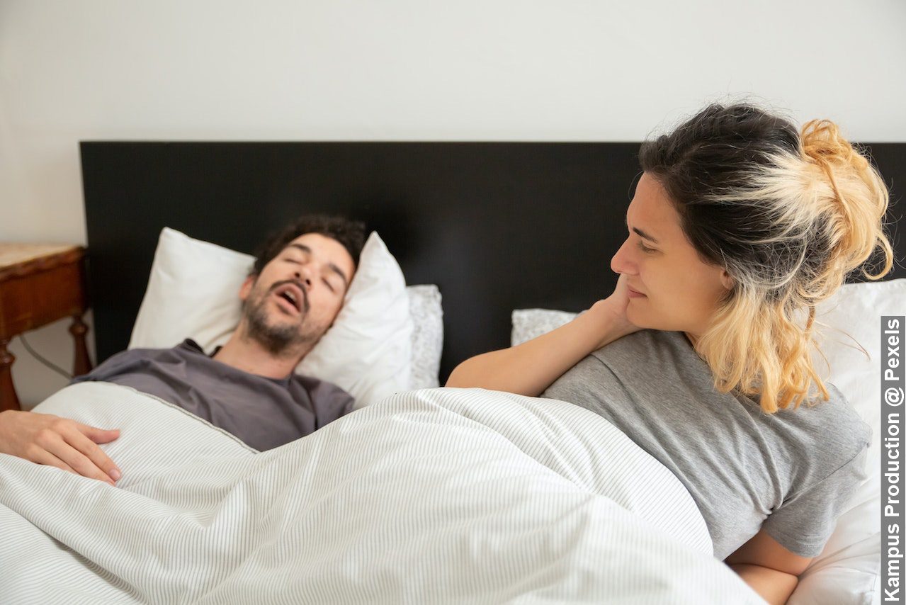 Woman lying on bed with a snoring man