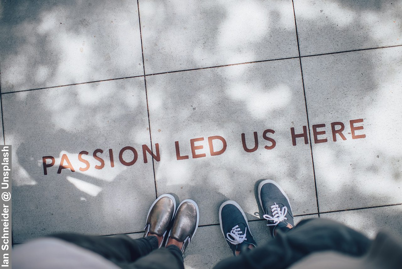 Passions led us here words on pavement with two sets of feet next to it