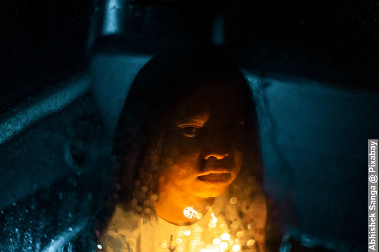 Through rainy glass window view of serious child with bright light