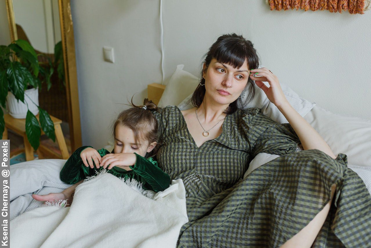 Tired mother with cute daughter resting on bed in cosy room