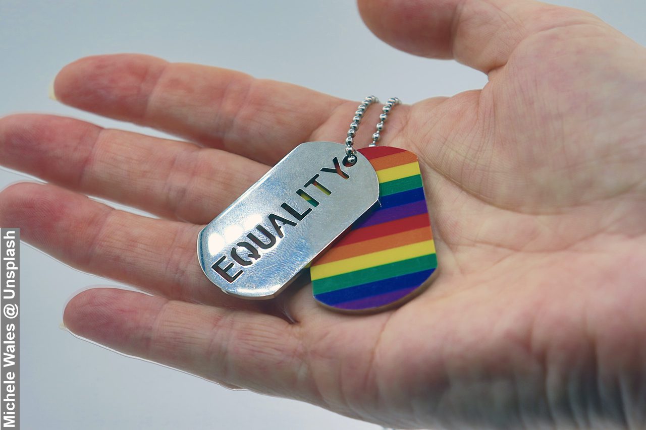A person holding a rainbow and equality dog tag in their hand