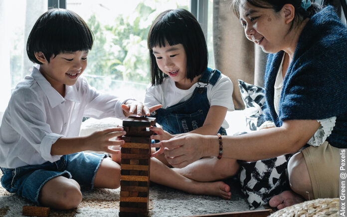 Little cute Asian siblings playing tower game with smiling grandmother
