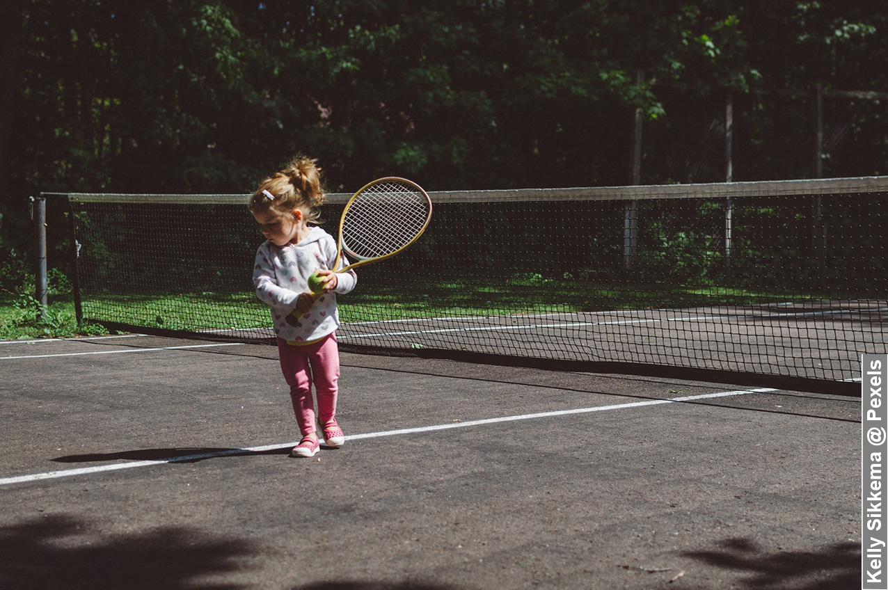 Child prodigy little girl on tennis court with racket in hand