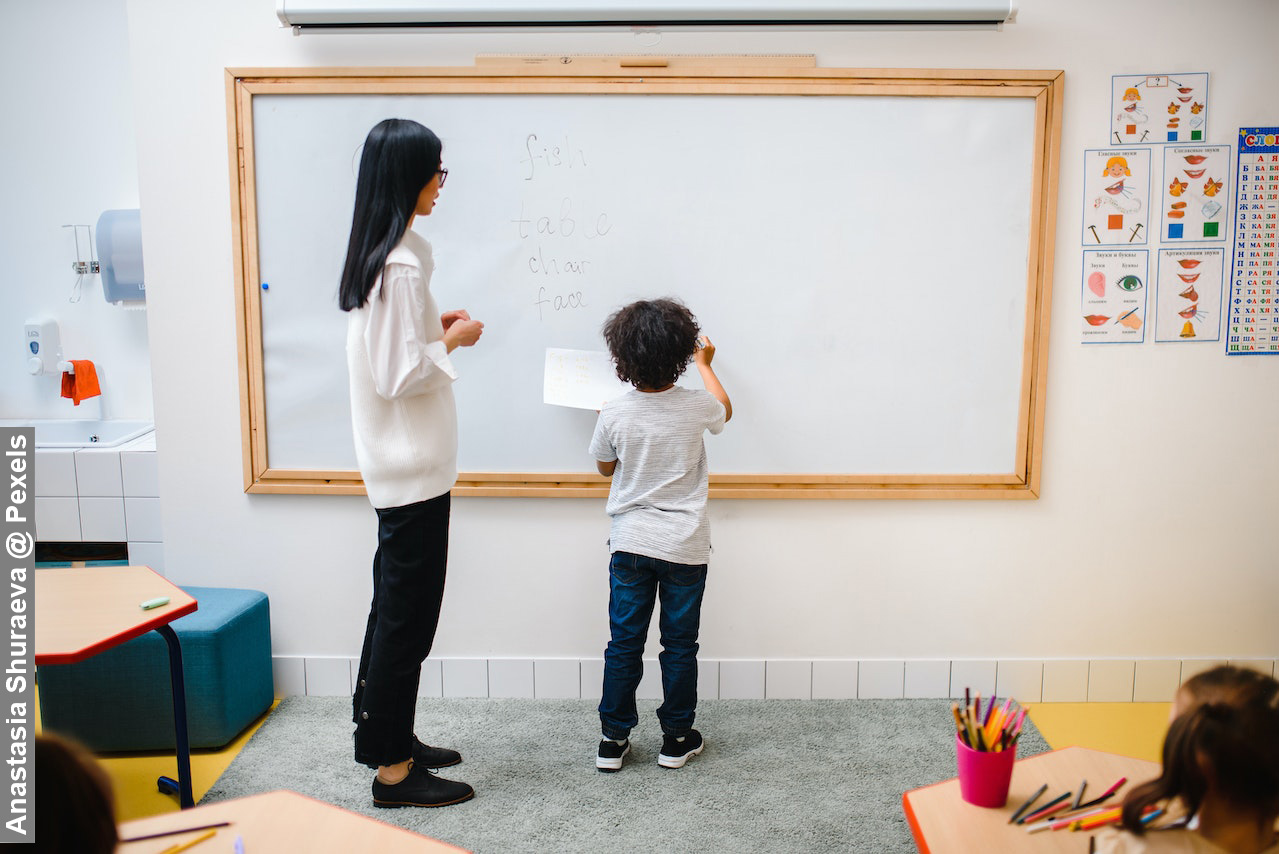 Female teacher with young child standing in front of whiteboard in classroom